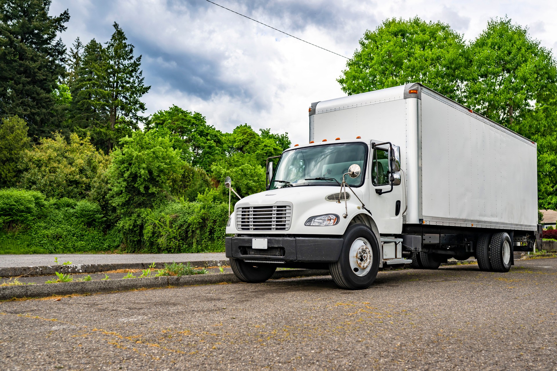 Day cab middle duty rig semi truck with long box trailer standing on the local road waiting for the next load